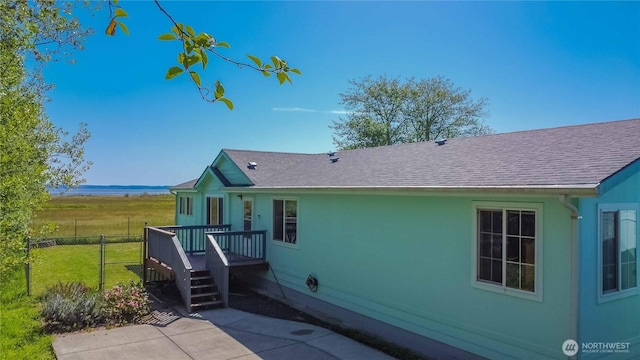 back of property featuring fence, a patio, a shingled roof, and a deck with water view