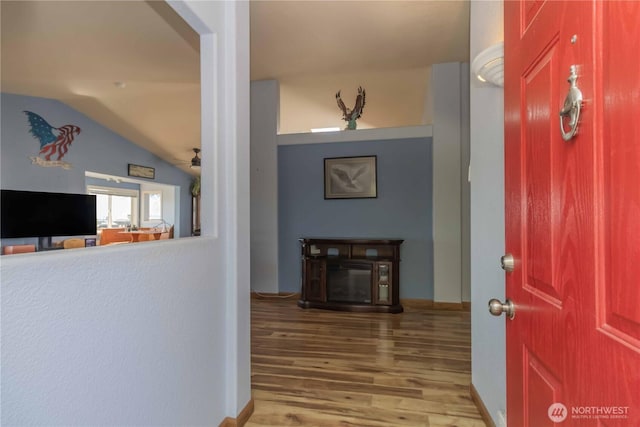 hallway with baseboards, vaulted ceiling, and wood finished floors