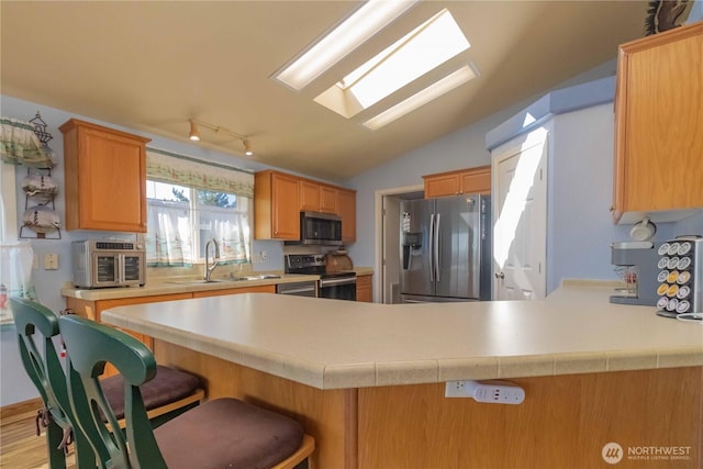 kitchen with a peninsula, light countertops, rail lighting, a sink, and appliances with stainless steel finishes