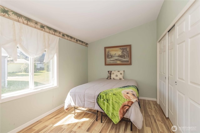 bedroom featuring a closet, baseboards, wood finished floors, and vaulted ceiling