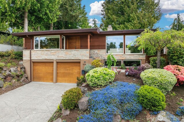 modern home with stone siding, a garage, a chimney, and driveway