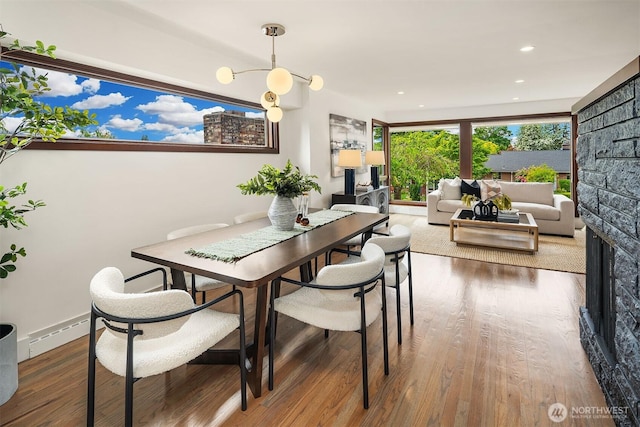 dining space with wood finished floors, a baseboard radiator, a fireplace, and recessed lighting