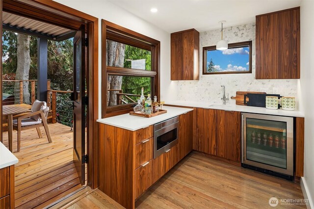 indoor bar with beverage cooler, stainless steel microwave, and light wood finished floors