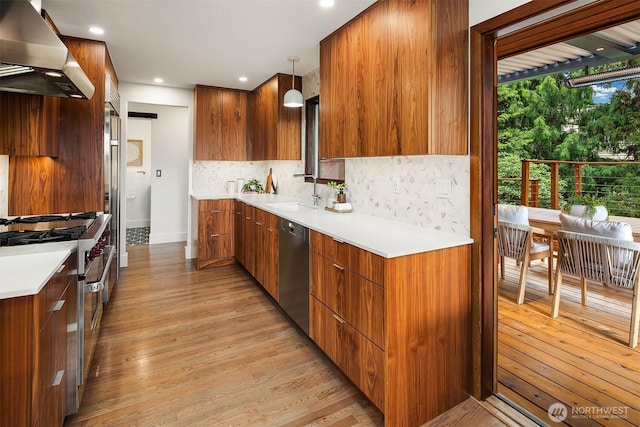kitchen featuring wall chimney range hood, stainless steel appliances, a sink, modern cabinets, and decorative backsplash