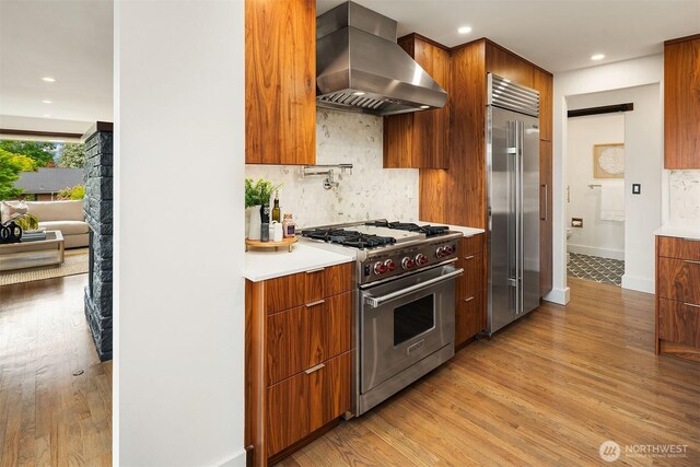 kitchen featuring premium appliances, wall chimney range hood, modern cabinets, light wood-style floors, and recessed lighting