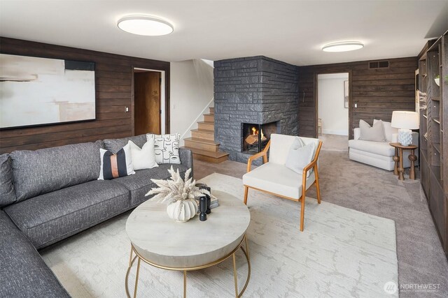 living room featuring wooden walls, a stone fireplace, stairway, and carpet flooring