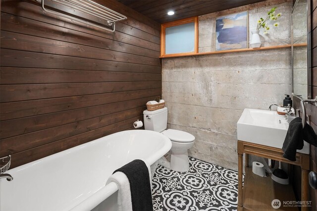 bathroom with a soaking tub, toilet, wooden walls, vanity, and tile patterned floors
