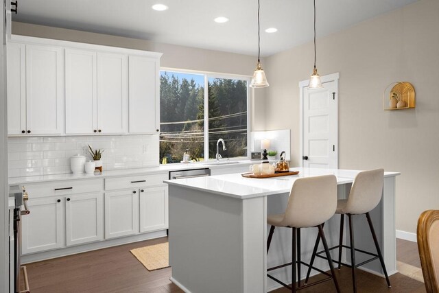 kitchen featuring backsplash, a kitchen island, a kitchen bar, a sink, and white cabinetry