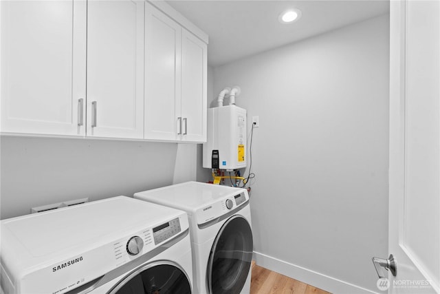 clothes washing area with washer and clothes dryer, light wood-type flooring, baseboards, cabinet space, and tankless water heater