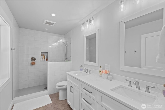 bathroom featuring toilet, a sink, a walk in shower, and visible vents