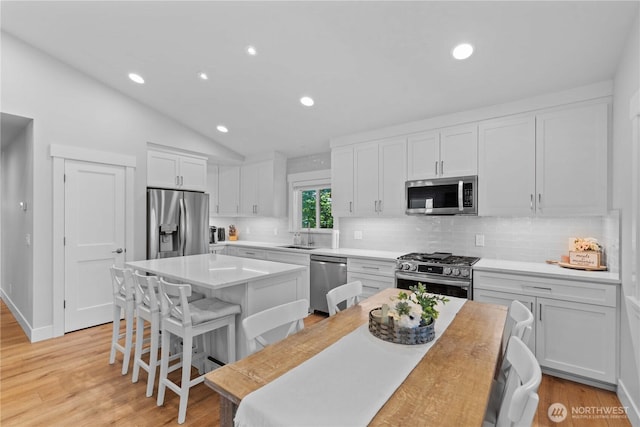 kitchen with a kitchen breakfast bar, stainless steel appliances, decorative backsplash, a kitchen island, and white cabinets