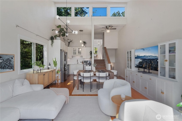 living area with ceiling fan, wood finished floors, a high ceiling, and stairway