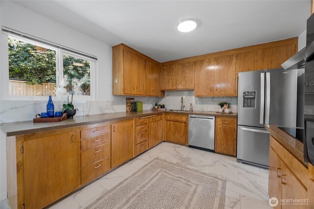 kitchen with brown cabinetry, marble finish floor, a sink, backsplash, and stainless steel appliances