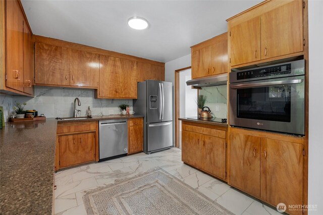kitchen featuring marble finish floor, dark countertops, under cabinet range hood, a sink, and appliances with stainless steel finishes