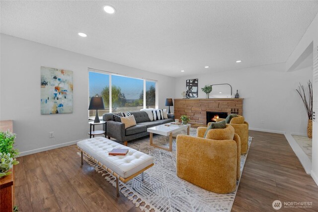 living area featuring baseboards, a textured ceiling, wood finished floors, and a fireplace
