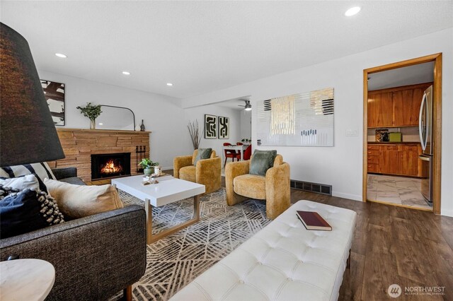 living room featuring visible vents, wood finished floors, baseboards, a warm lit fireplace, and recessed lighting