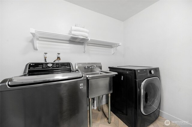 clothes washing area featuring separate washer and dryer, laundry area, a sink, and baseboards