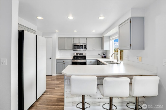 kitchen with gray cabinets, stainless steel appliances, a sink, a peninsula, and wood finished floors