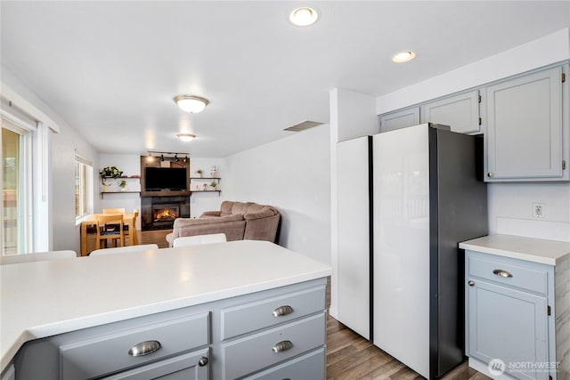 kitchen with light countertops, gray cabinetry, a large fireplace, visible vents, and freestanding refrigerator