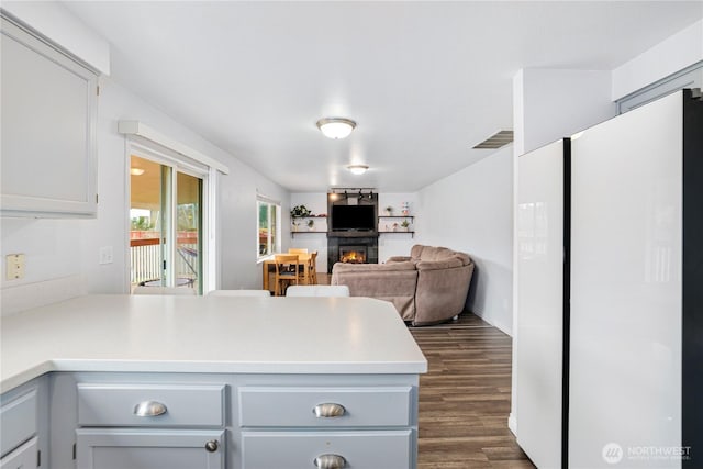 kitchen featuring light countertops, visible vents, a peninsula, dark wood finished floors, and a lit fireplace