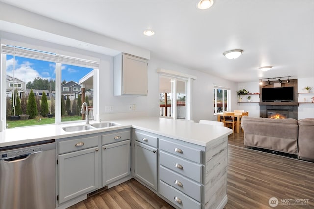 kitchen featuring dark wood-type flooring, a large fireplace, a sink, dishwasher, and a peninsula