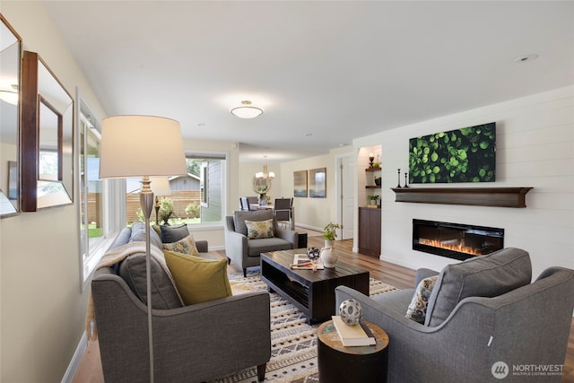living area with a notable chandelier, a glass covered fireplace, baseboards, and wood finished floors