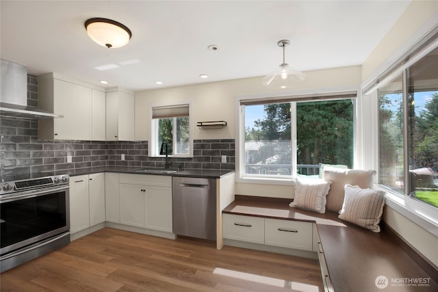kitchen featuring wall chimney exhaust hood, a sink, dark countertops, and appliances with stainless steel finishes