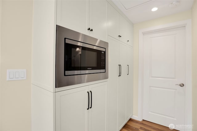 interior details featuring stainless steel microwave, recessed lighting, white cabinetry, and light wood-type flooring