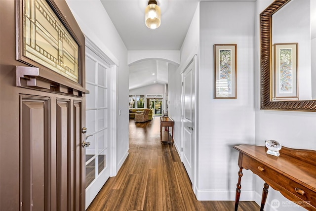 hallway with arched walkways, baseboards, dark wood-style floors, and lofted ceiling