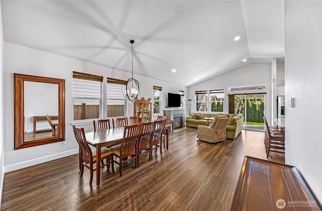 dining area with a glass covered fireplace, baseboards, an inviting chandelier, vaulted ceiling, and dark wood-type flooring