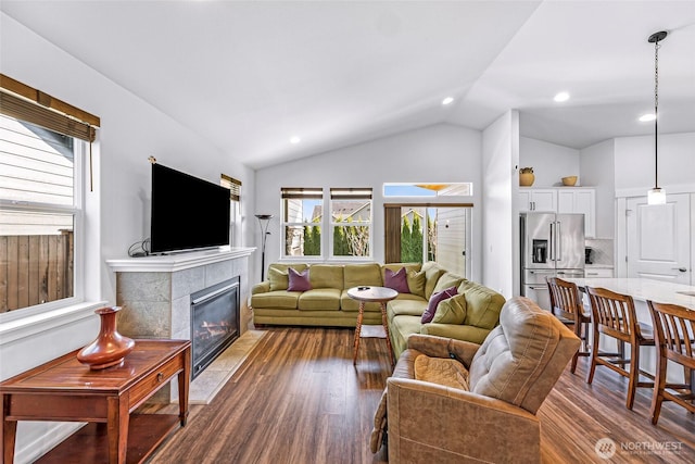 living area featuring dark wood-type flooring, recessed lighting, a tiled fireplace, and vaulted ceiling