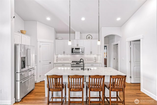 kitchen with a kitchen breakfast bar, tasteful backsplash, arched walkways, appliances with stainless steel finishes, and a sink