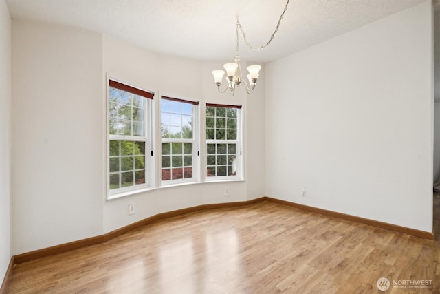 empty room with baseboards, wood finished floors, and a chandelier