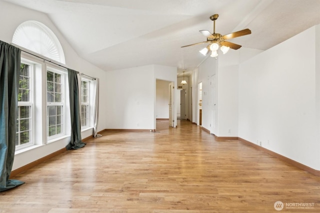 empty room featuring light wood-type flooring, a ceiling fan, baseboards, and vaulted ceiling