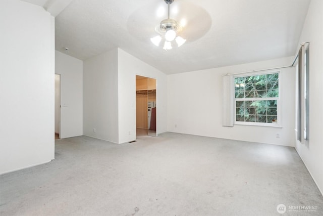 unfurnished bedroom featuring carpet floors, a ceiling fan, a walk in closet, and vaulted ceiling