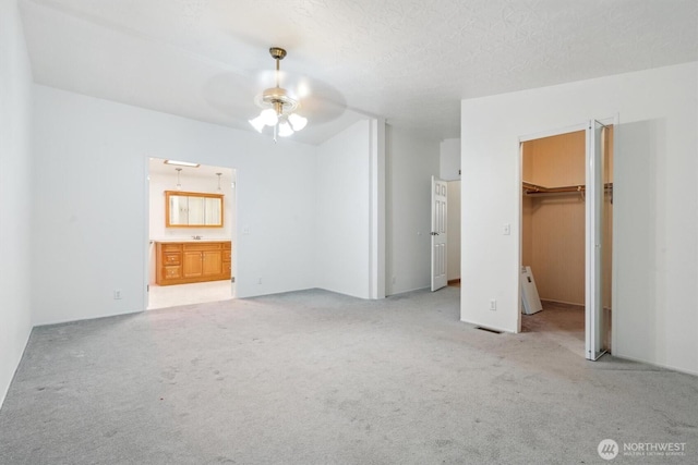 unfurnished bedroom featuring a walk in closet, light carpet, ensuite bath, and visible vents