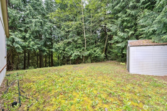 view of yard with a storage shed, a wooded view, and an outdoor structure