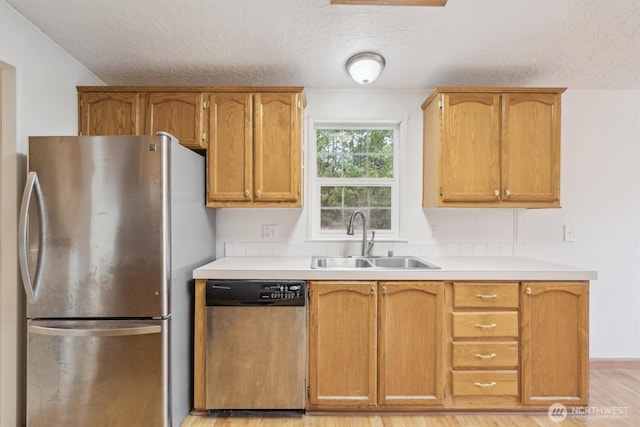 kitchen featuring a sink, appliances with stainless steel finishes, light wood-type flooring, and light countertops