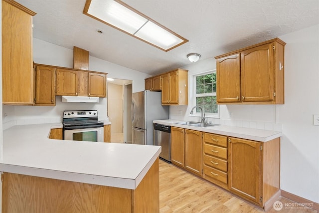 kitchen with light countertops, under cabinet range hood, a sink, vaulted ceiling, and stainless steel appliances
