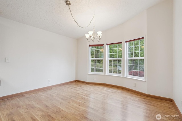 unfurnished room with an inviting chandelier, baseboards, a textured ceiling, and wood finished floors