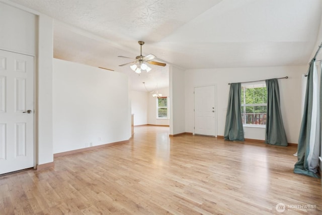 spare room with light wood-type flooring, ceiling fan with notable chandelier, lofted ceiling, and a healthy amount of sunlight