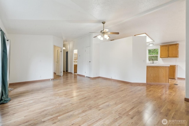 unfurnished living room featuring a ceiling fan, vaulted ceiling, a sink, and light wood finished floors