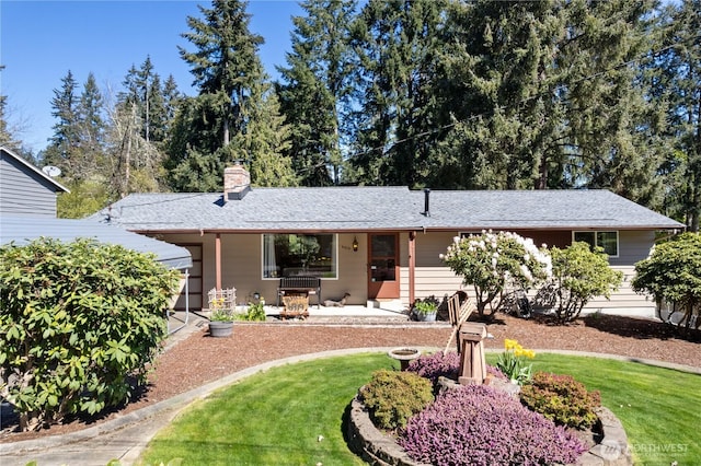 ranch-style house featuring a patio, a shingled roof, a front lawn, and a chimney