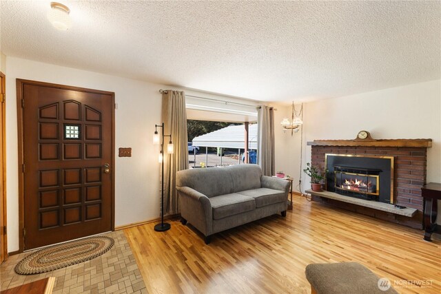 living room with a brick fireplace, a textured ceiling, and light wood finished floors