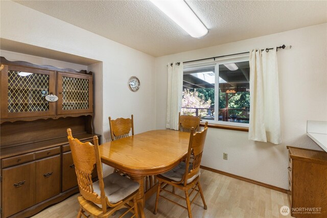 dining space featuring baseboards, a textured ceiling, and light wood-style flooring