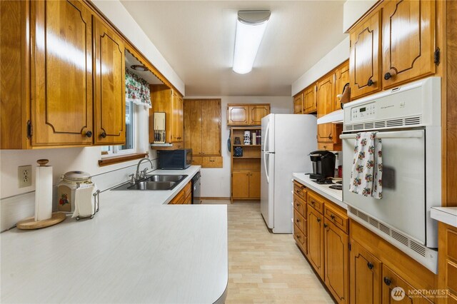 kitchen featuring brown cabinetry, light countertops, under cabinet range hood, a sink, and black appliances