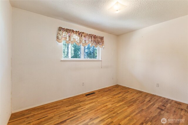 spare room with visible vents, a textured ceiling, baseboards, and wood finished floors
