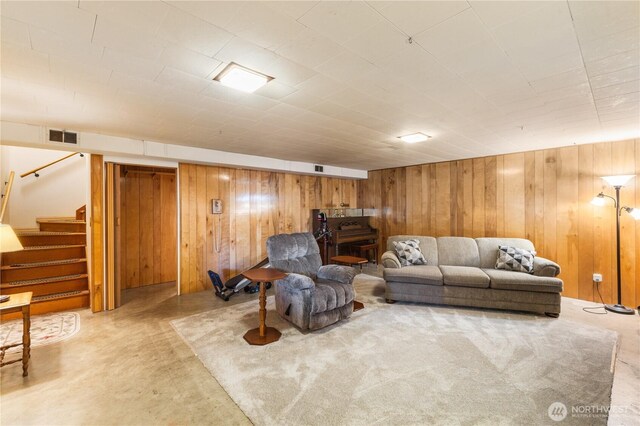 living room with stairway, concrete flooring, wood walls, and visible vents