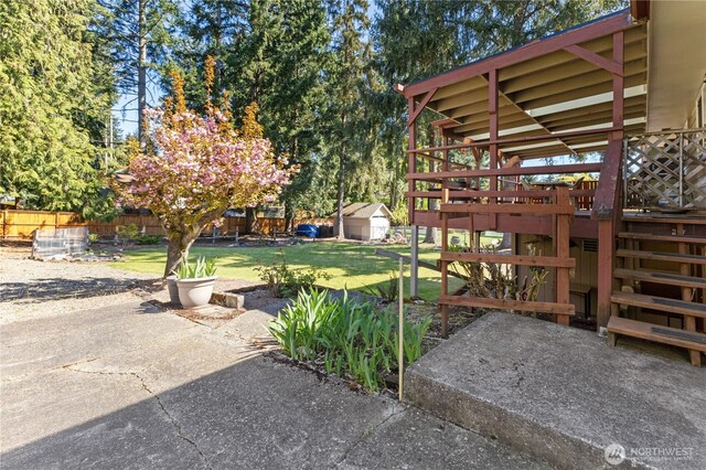 view of yard featuring a wooden deck, an outbuilding, stairway, fence, and a patio