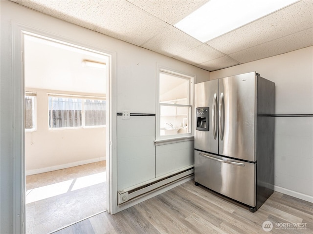 kitchen featuring a paneled ceiling, stainless steel refrigerator with ice dispenser, light wood-style flooring, and baseboard heating
